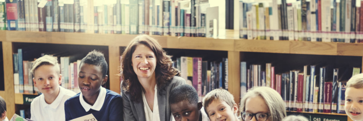 White female teacher and mixed primary pupils in library