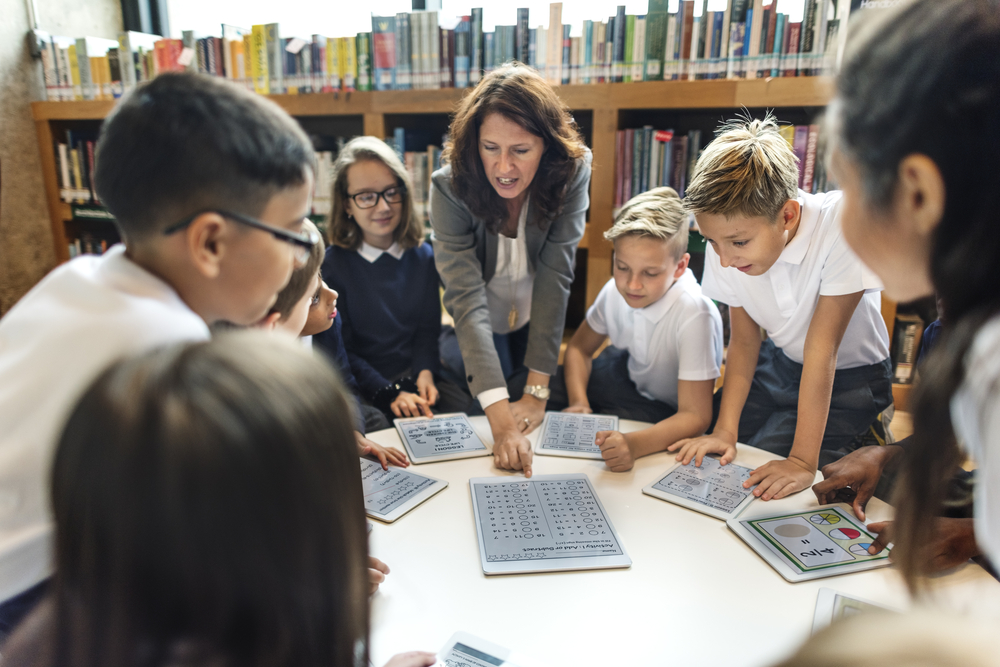 White female teacher with mixed primary children round table